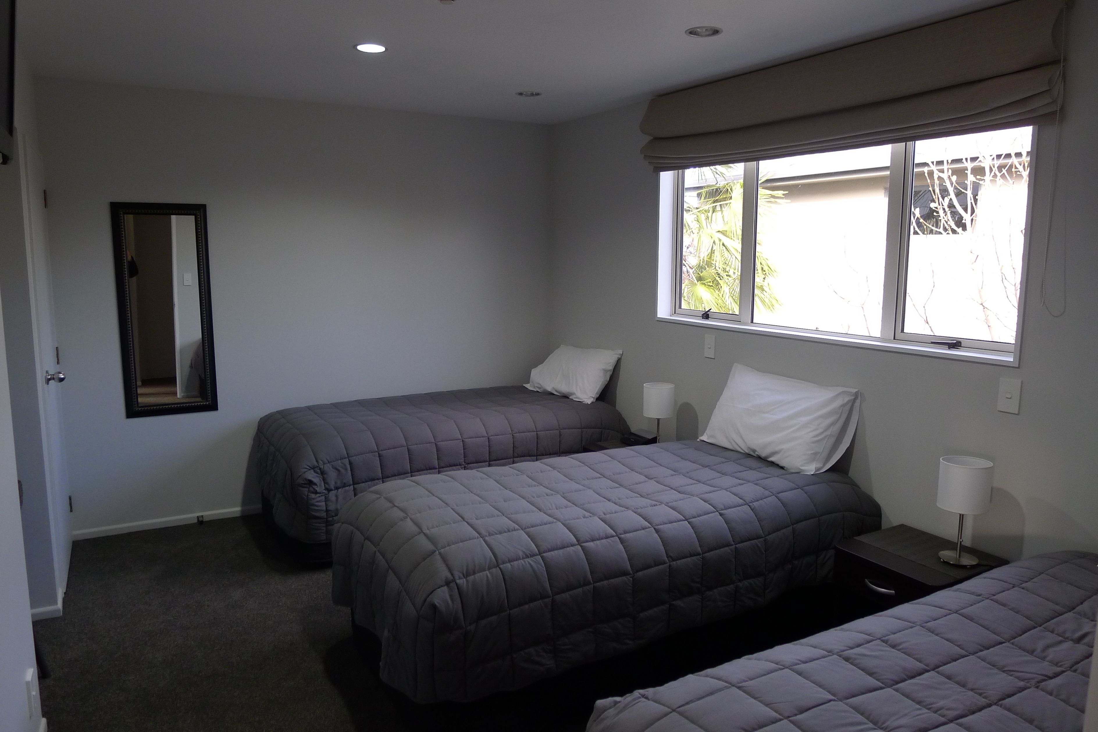 Un dormitorio con dos camas, una ventana con cortinas, una mesita de noche con lámpara y un espejo en la pared.