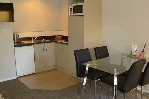 Cocina compacta con microondas, cafetera y pileta. Hay una mesa de vidrio con cuatro sillas.