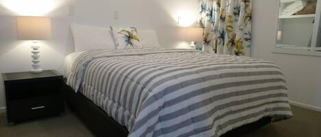 A hotel room with a bed, two bedside lamps, a nightstand, a mirror, and a floral curtain.