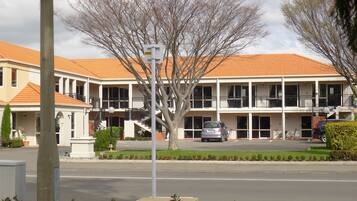 A two-story building with a tiled roof, multiple balconies, and a parking area in front.