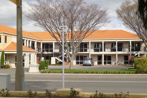 A two-story building with a tiled roof, multiple balconies, and a parking area in front.