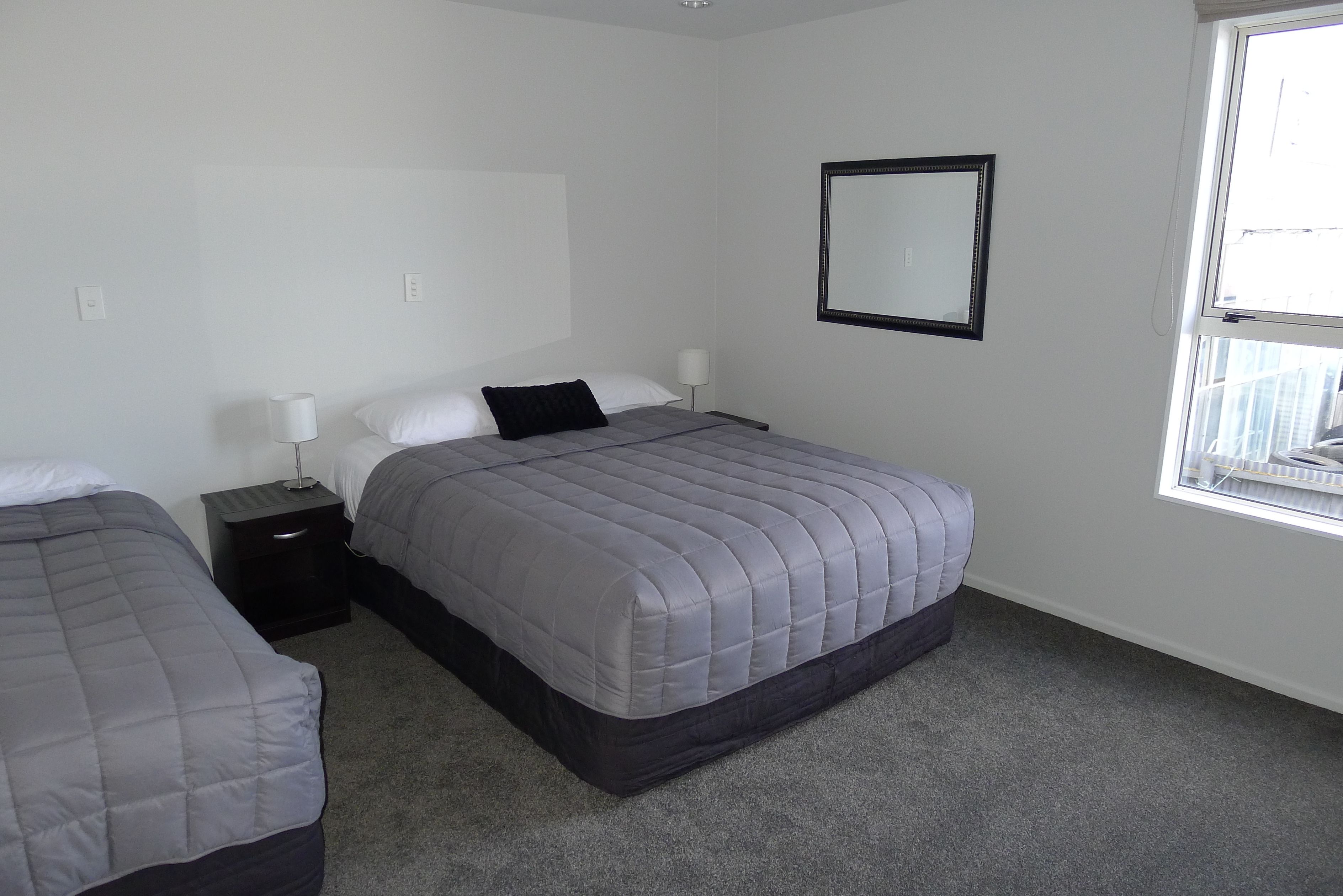 A bedroom with two beds, a nightstand, a lamp, a mirror, and a window.
