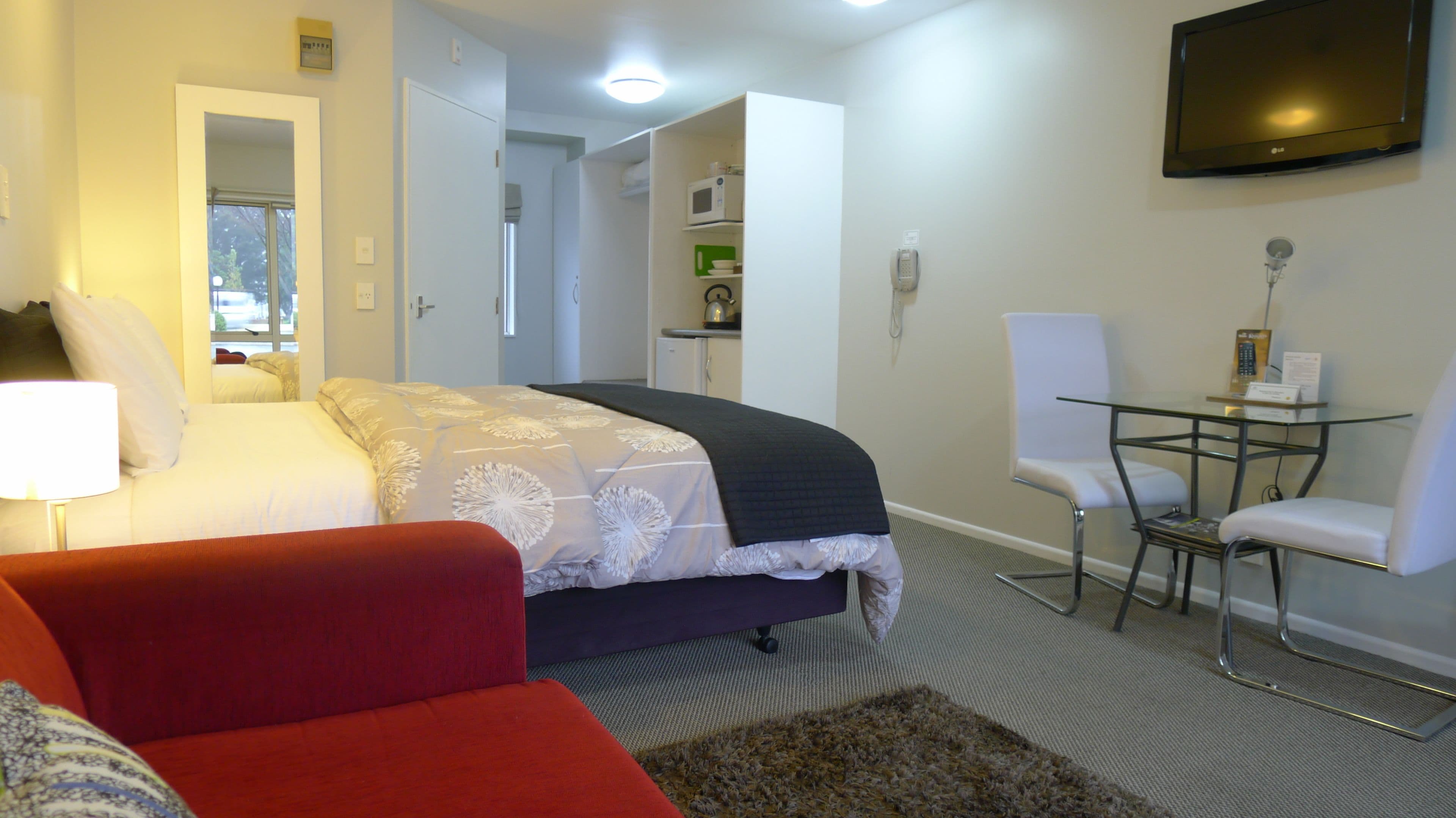 Hotelkamer met een bed, een rode bank, een kleintje tafeltje met een stoel, een tv aan de muur en een magnetron in de kitchenette.