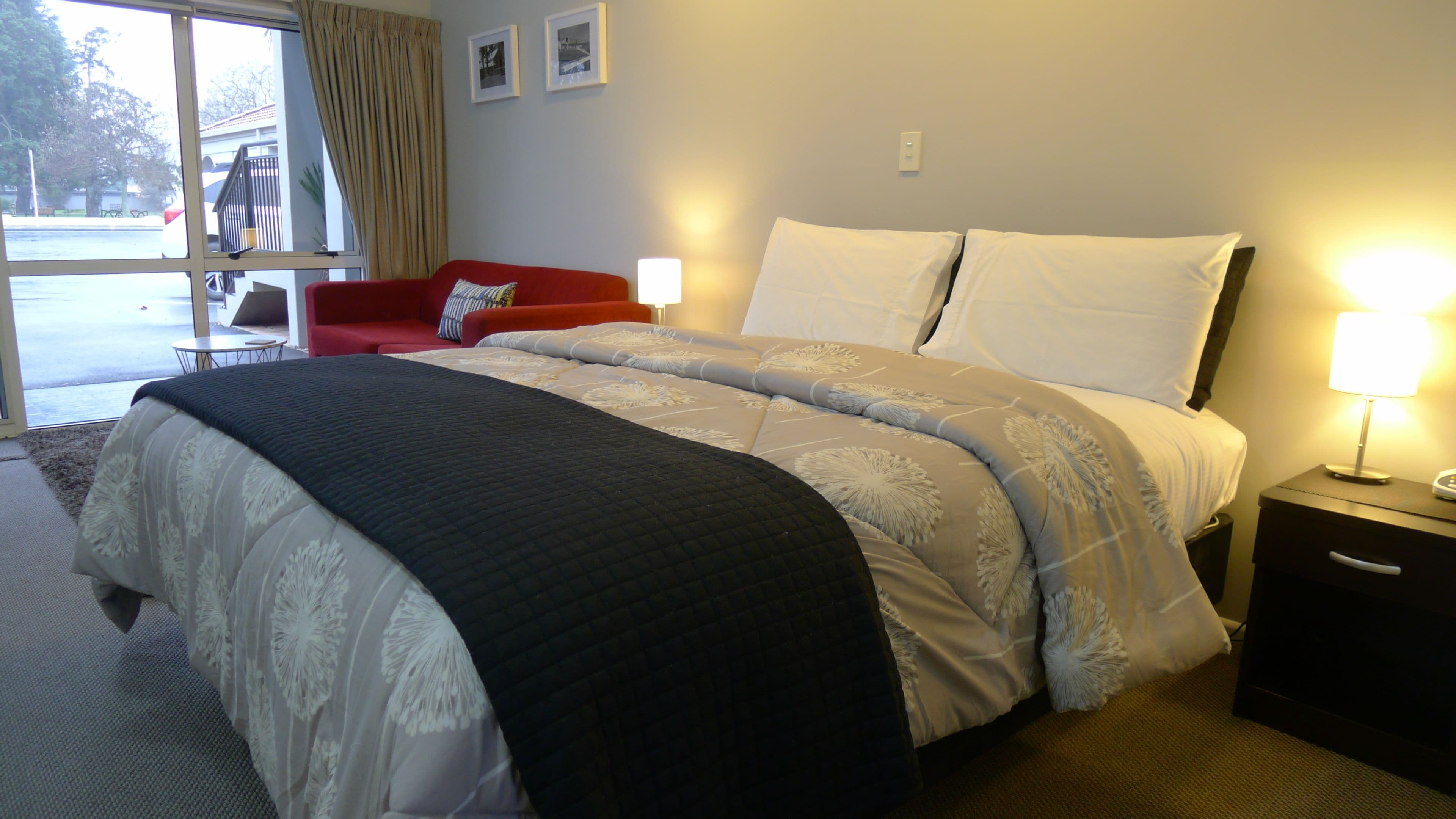 Habitación de hotel con una cama grande, dos lámparas de noche, un sillón rojo y una ventana con cortinas.