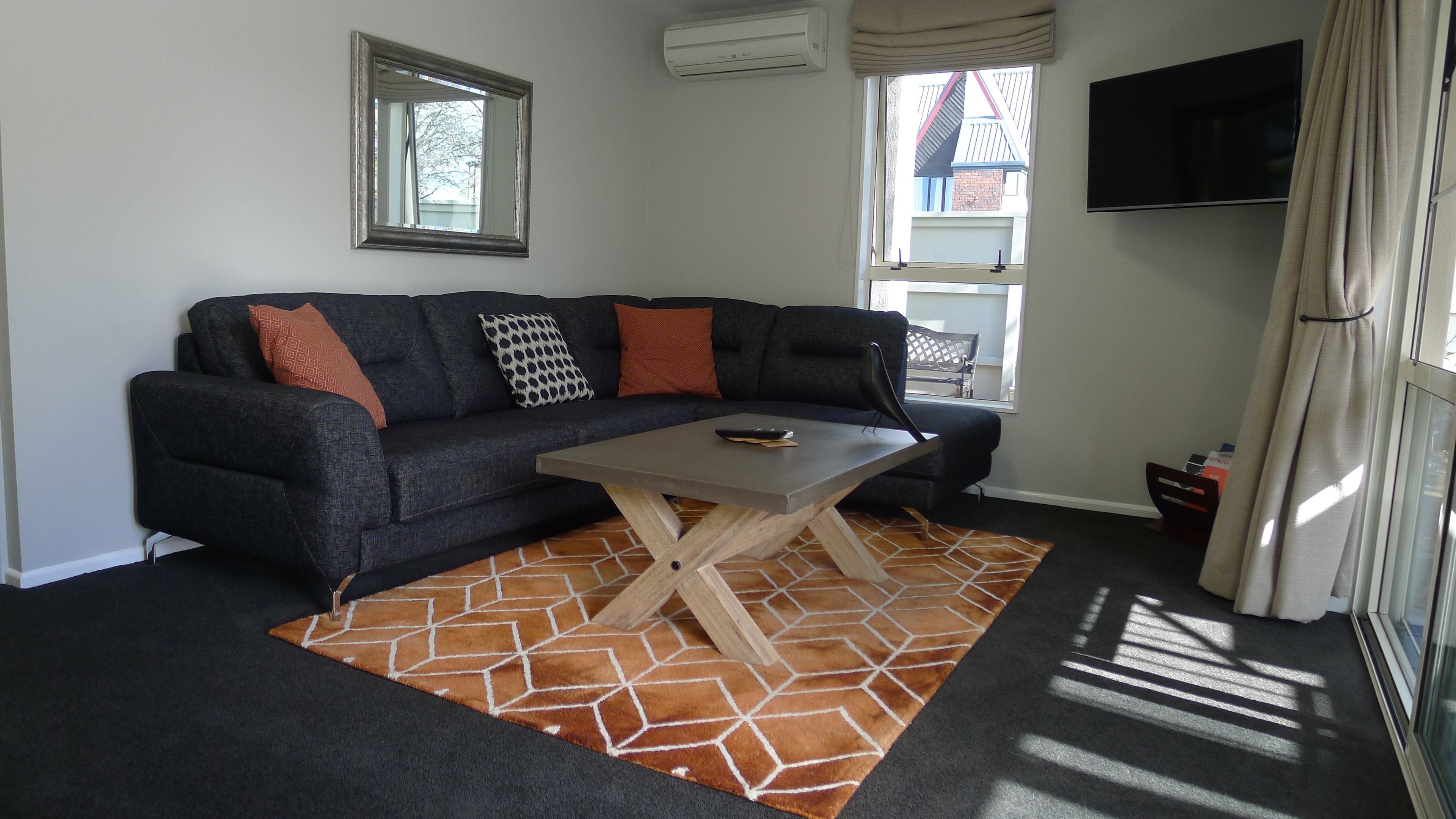 Een woonkamer met een donkere bank, een houten bijzettafeltje en een kamerkleed met een patroon.