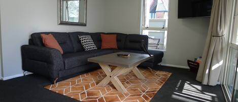 Ein Wohnzimmer mit einem dunklen Sofa, einem Holztisch und einem gemusterten Teppich.