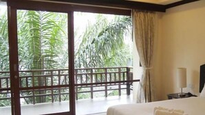 A hotel room with a large sliding glass door leading to a balcony with a view of lush greenery. - Summer Inn (Koh Samui)