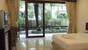 A hotel room with a bed, a TV, and a view of a garden through a glass door. - Summer Inn (Koh Samui)