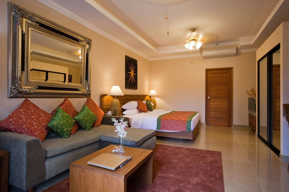 Ein Hotelzimmer mit Bett, einer Couch, einem Couchtisch, einem großen Spiegel und einer Tür.