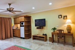 A living room with a ceiling fan, a flat-screen TV, a wooden desk, a chair, a lamp, and a refrigerator. - Baan Souy Resort (Pattaya)