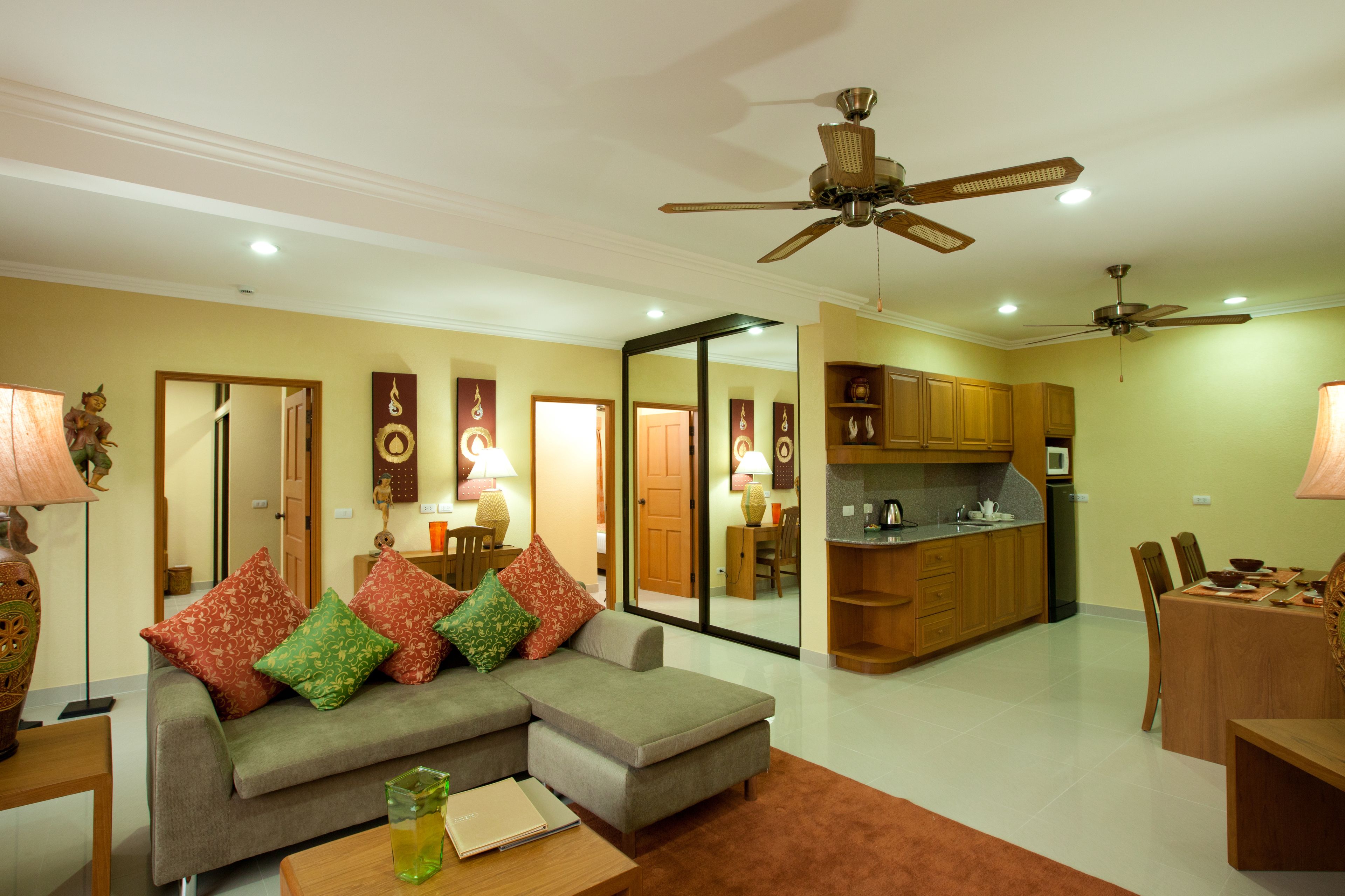 A living room with a sofa, coffee table, and dining area with chairs and a table. There is a kitchen area with cabinets and a refrigerator.
