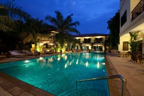 A swimming pool with lounge chairs and palm trees, surrounded by a building with balconies and outdoor seating. - Baan Souy Resort (Pattaya)