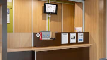 En receptionsdisk med en digital skærm, kasseapparat og informationsplakater.