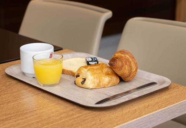 Una bandeja con un croissant, un vaso de jugo de naranja y una taza blanca sobre una mesa de madera.