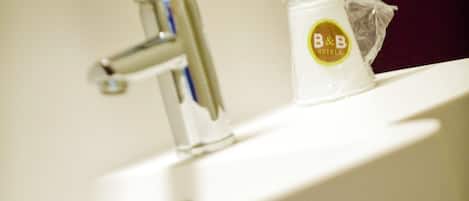 Un lavamanos con toallero, dispensador de jabón y una bolsa de plástico con el logotipo del hotel.