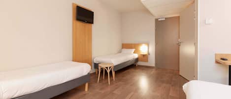 A hotel room with two single beds, a small wooden stool, a wall-mounted TV, and a bedside lamp.