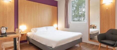 A modern hotel room with a bed, desk, chair, and a large mirror.