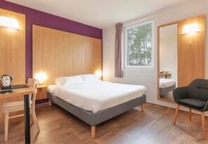 A modern hotel room with a bed, desk, chair, and a large mirror.