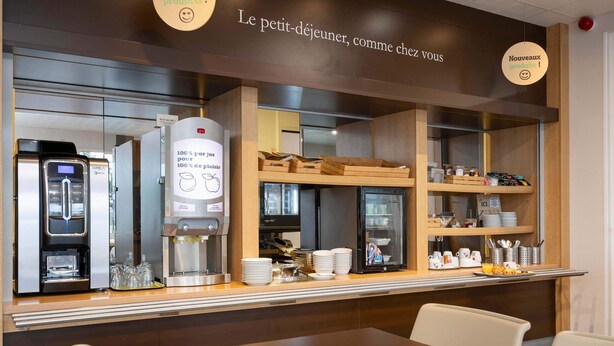 A café with a coffee machine, a refrigerator, and a display of breakfast items.