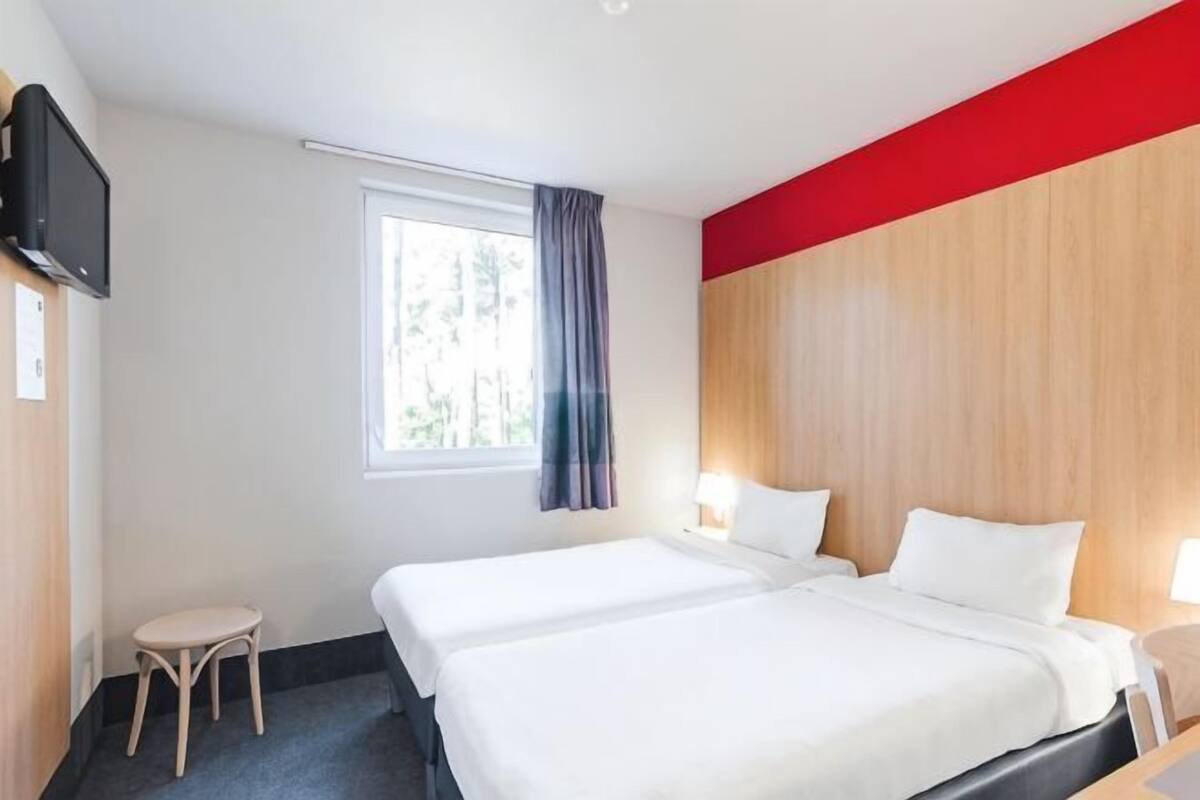 Hotellihuone, jossa on kaksi sänkyä, televisio, ikkuna verhoilla ja punainen tehosteseinä.