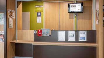 Un mostrador de recepción con un cartel de 'Welcome', certificados enmarcados y una pantalla digital.