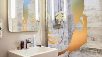 A bathroom with a large mirror, a shower, and a sink with toiletries.