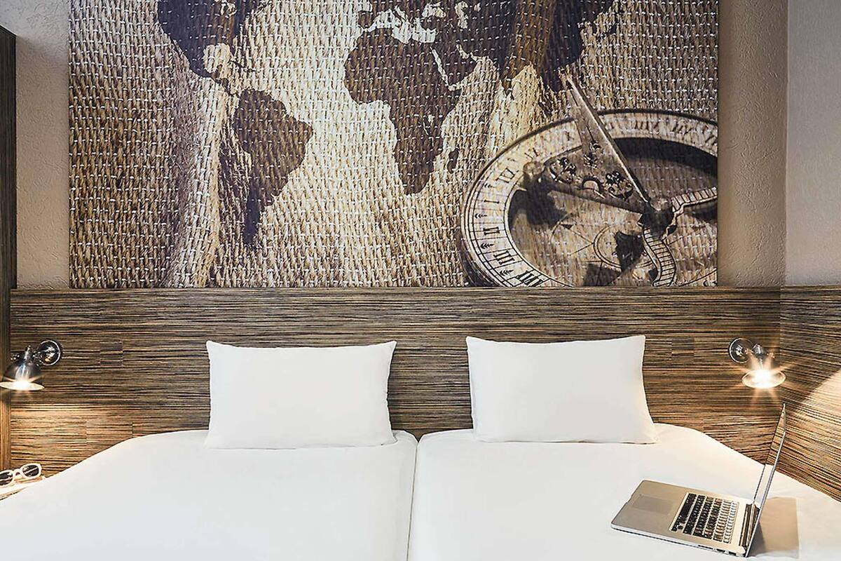 Une chambre d’hôtel avec une grande carte du monde et une horloge au mur, un lit avec du linge de lit blanc et un ordinateur portable posé sur le lit.