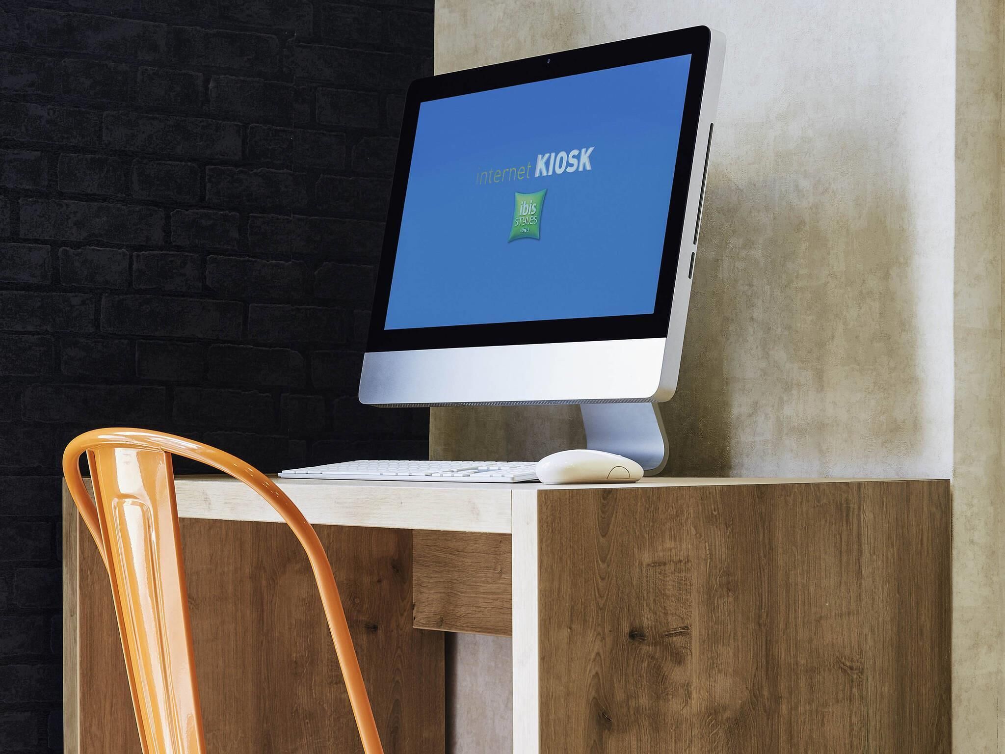 A desktop computer with a monitor displaying 'internet KIOSK' on a wooden desk against a brick wall.