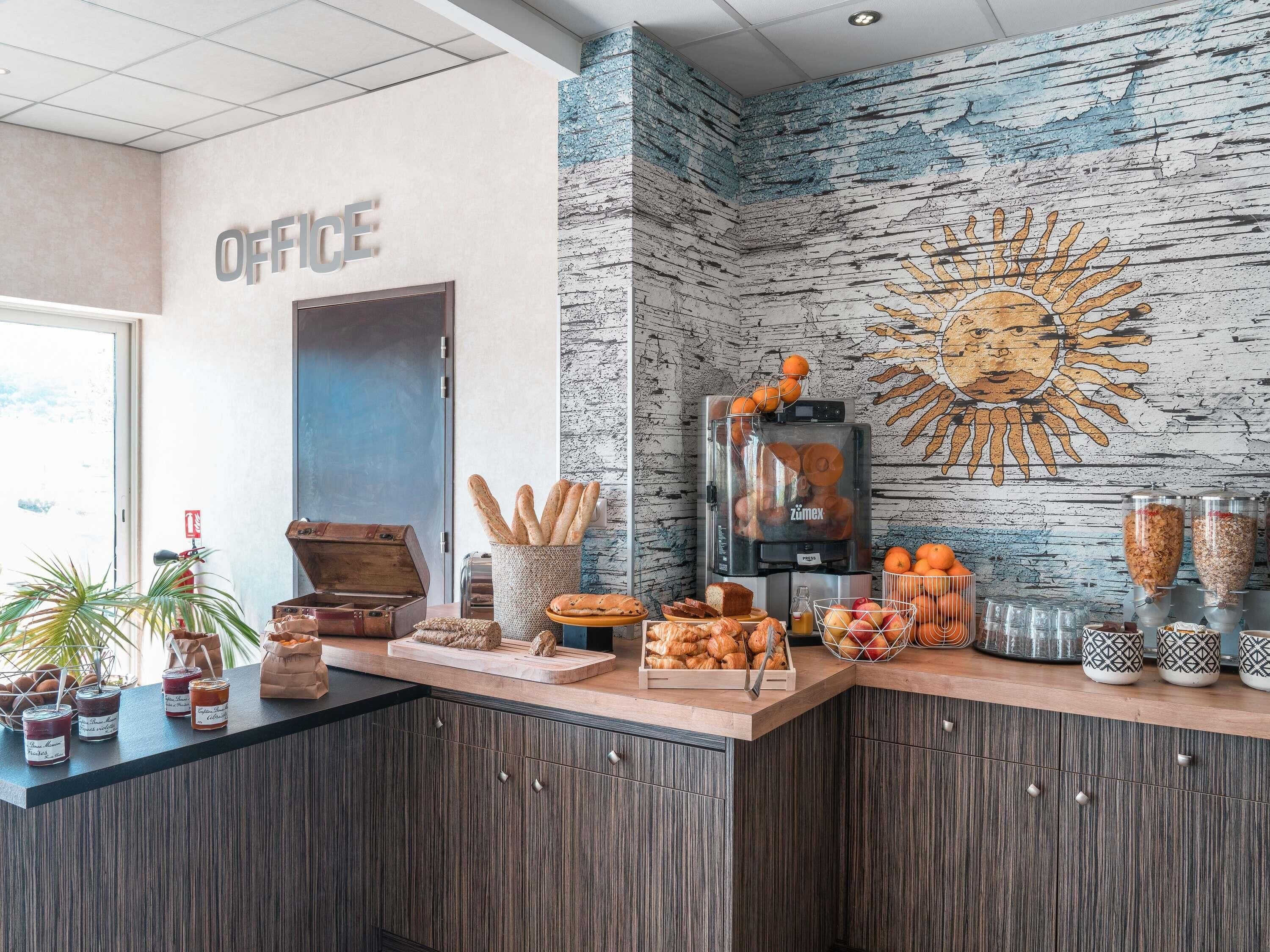 Zona de recepción con mostrador que exhibe pasteles, una máquina de café y un mural en la pared.