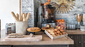 Una vitrina de panadería con diferentes panes y pasteles, una máquina de café y un mural decorativo con un motivo de sol en la pared.