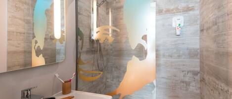 A bathroom with a large mirror, a shower with a glass door, and a sink with a toothbrush holder.
