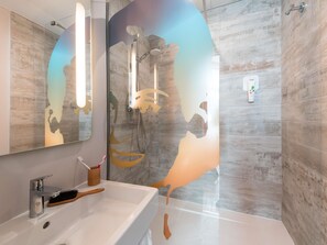 Une salle de bain avec un grand miroir, une douche avec une porte en verre et un lavabo doté d’un porte-brosse à dents.