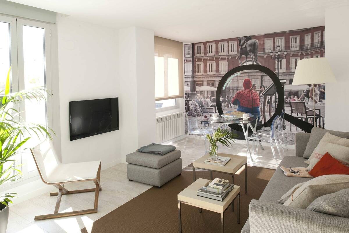 Un salon moderne comprenant un canapé, un pouf, une table basse et un téléviseur fixé au mur.