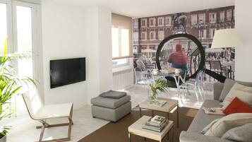 Una sala de estar moderna con sofá, reposapiés, mesa de centro y televisor montado en la pared.