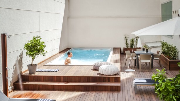 Una terraza de madera con un jacuzzi, sillas de descanso y una mesa con sillas.