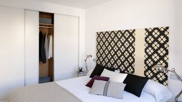 Un dormitorio con cama, armario, mesita de noche con lámpara y una pared con estampado floral.