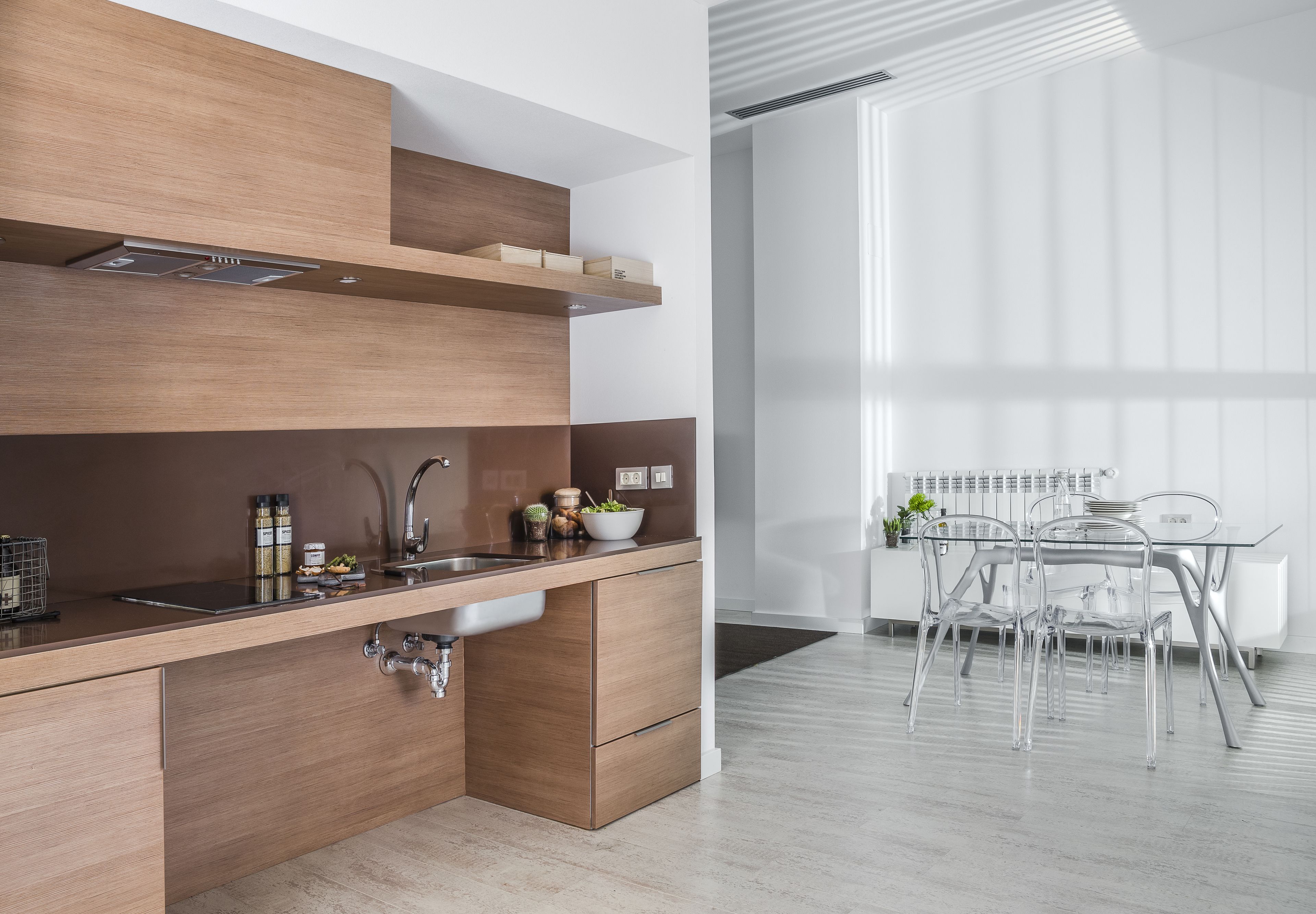 Uma cozinha moderna com armários de madeira, uma pia de aço inoxidável e uma área de jantar com mesa e cadeiras de vidro.