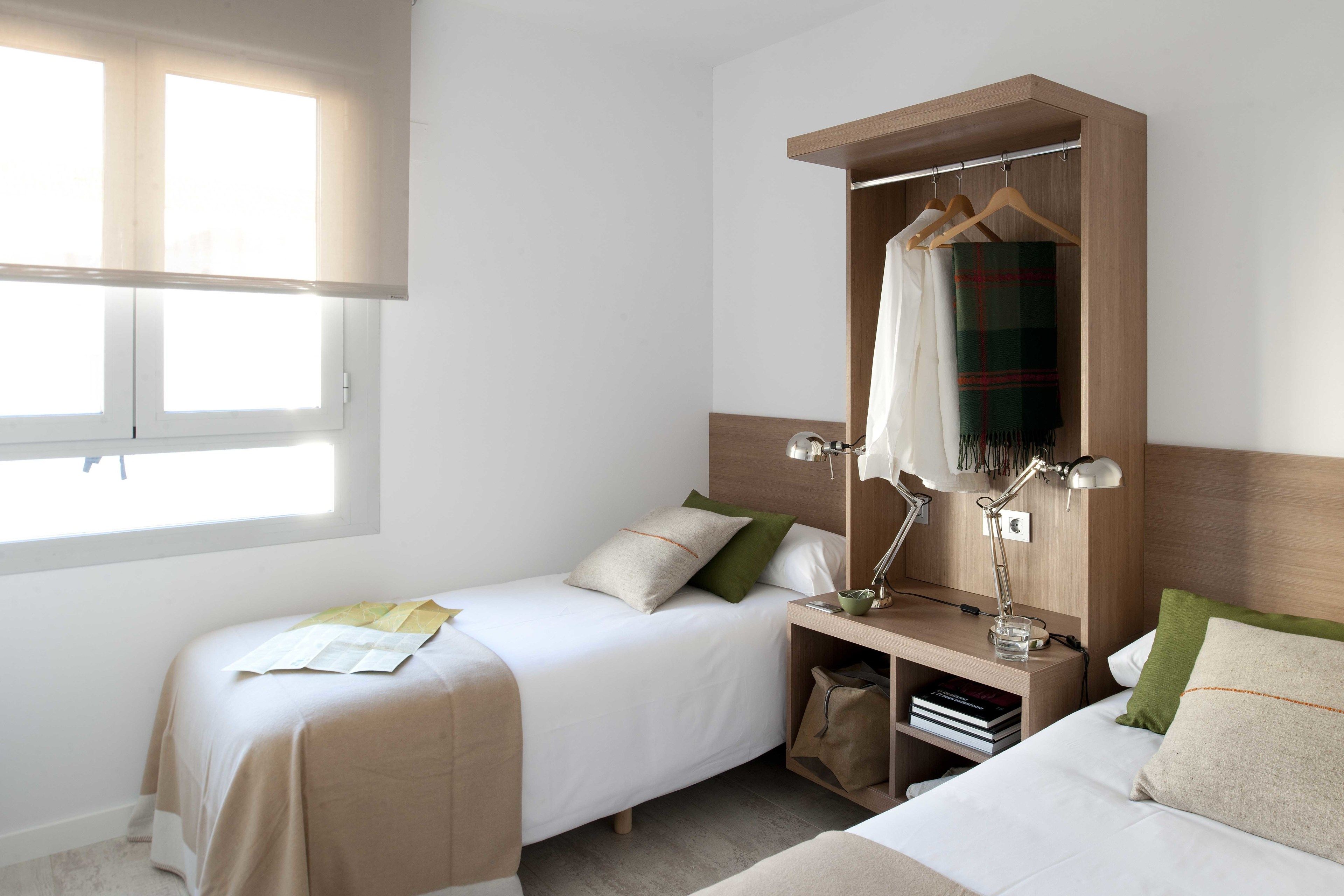 Habitación de hotel con dos camas, un armario, una mesita de noche con lámpara y una ventana.