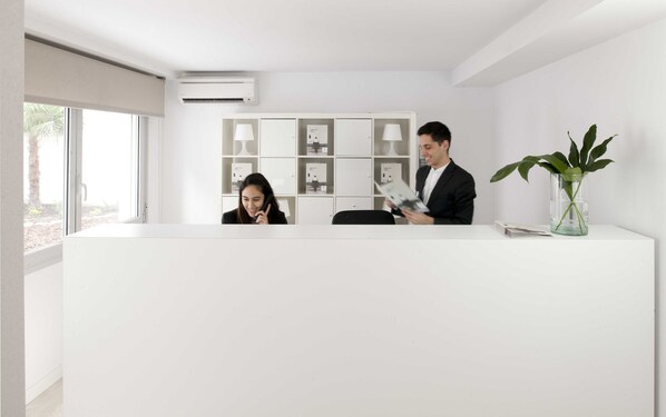 Un área de recepción con un escritorio blanco, una planta en maceta y un aire acondicionado instalado en la pared.