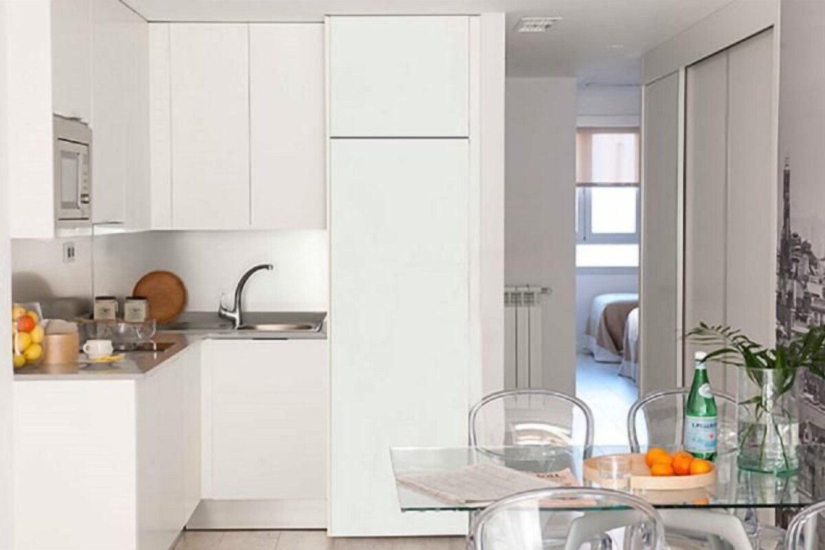 A compact kitchen with white cabinets, a sink, and a glass dining table with chairs.