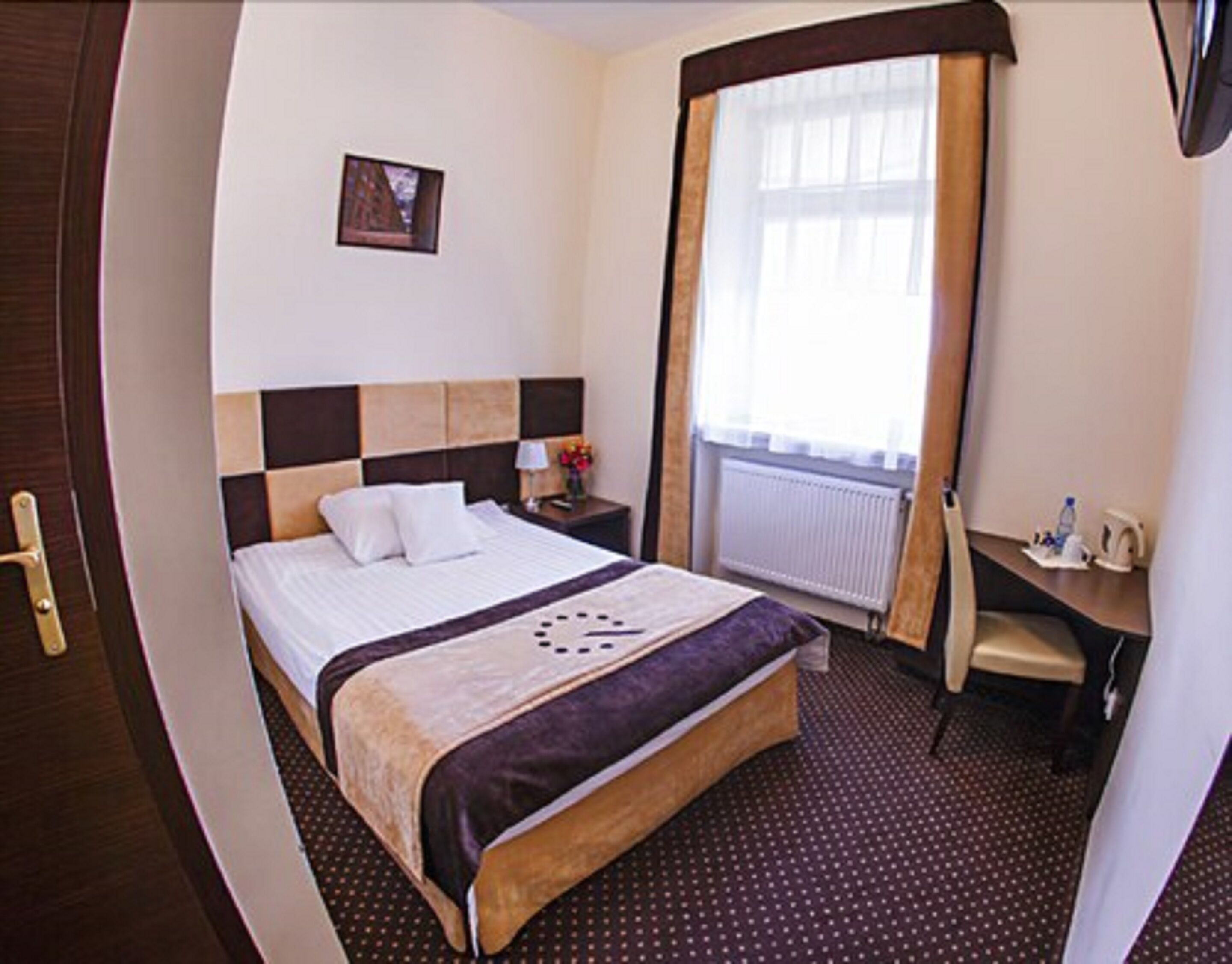 A hotel room with a bed, a desk, a chair, a picture on the wall, and a window with curtains.