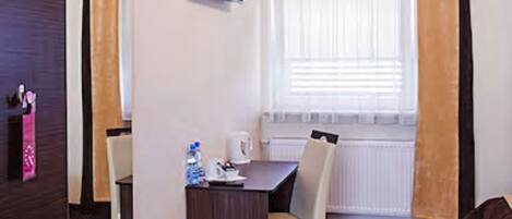 Une chambre d’hôtel de taille réduite, comprenant un lit, un bureau, une chaise, une télévision et une fenêtre avec des rideaux.
