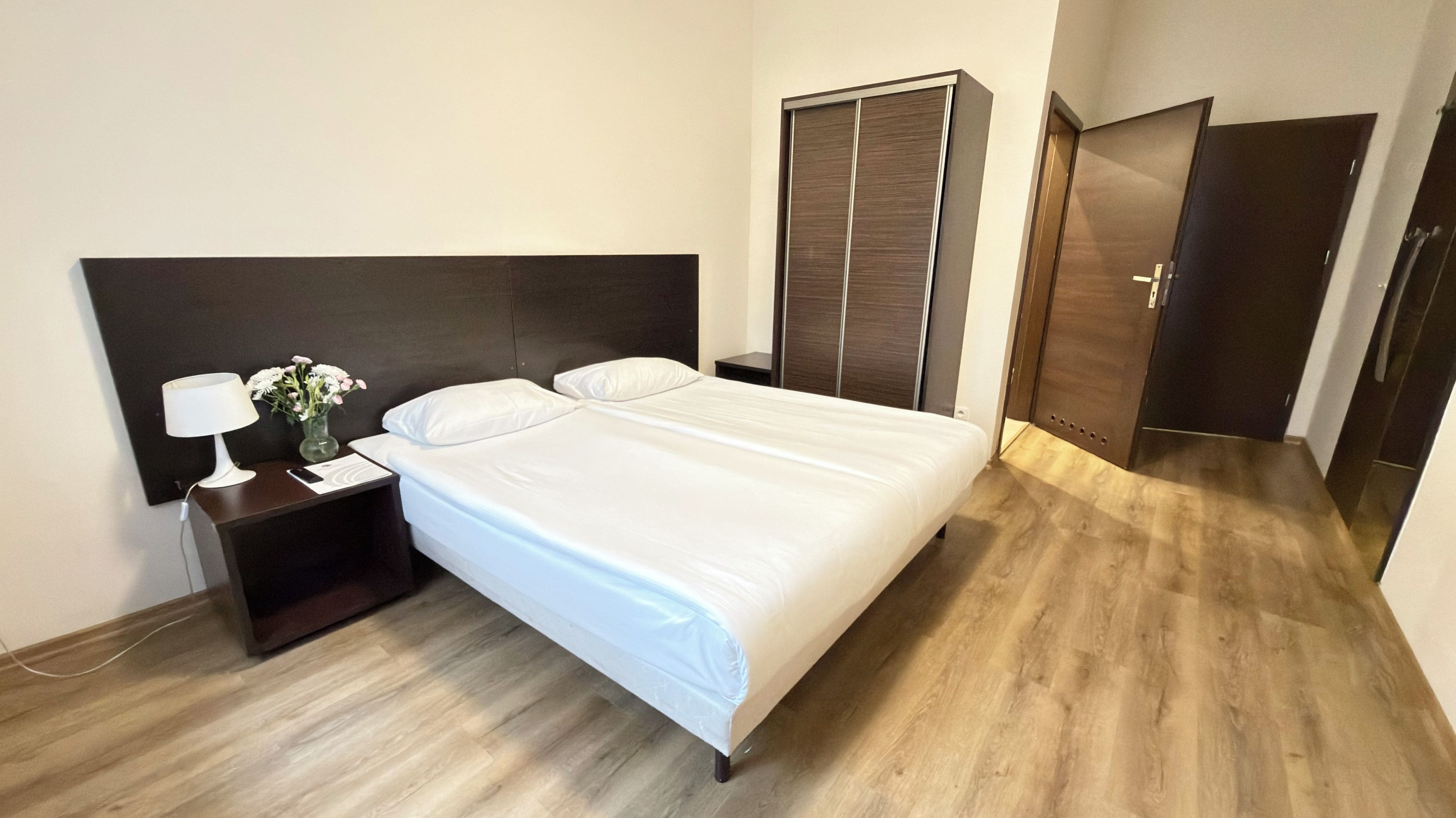 Una habitación de hotel con cama, mesita de noche, lámpara y armario.