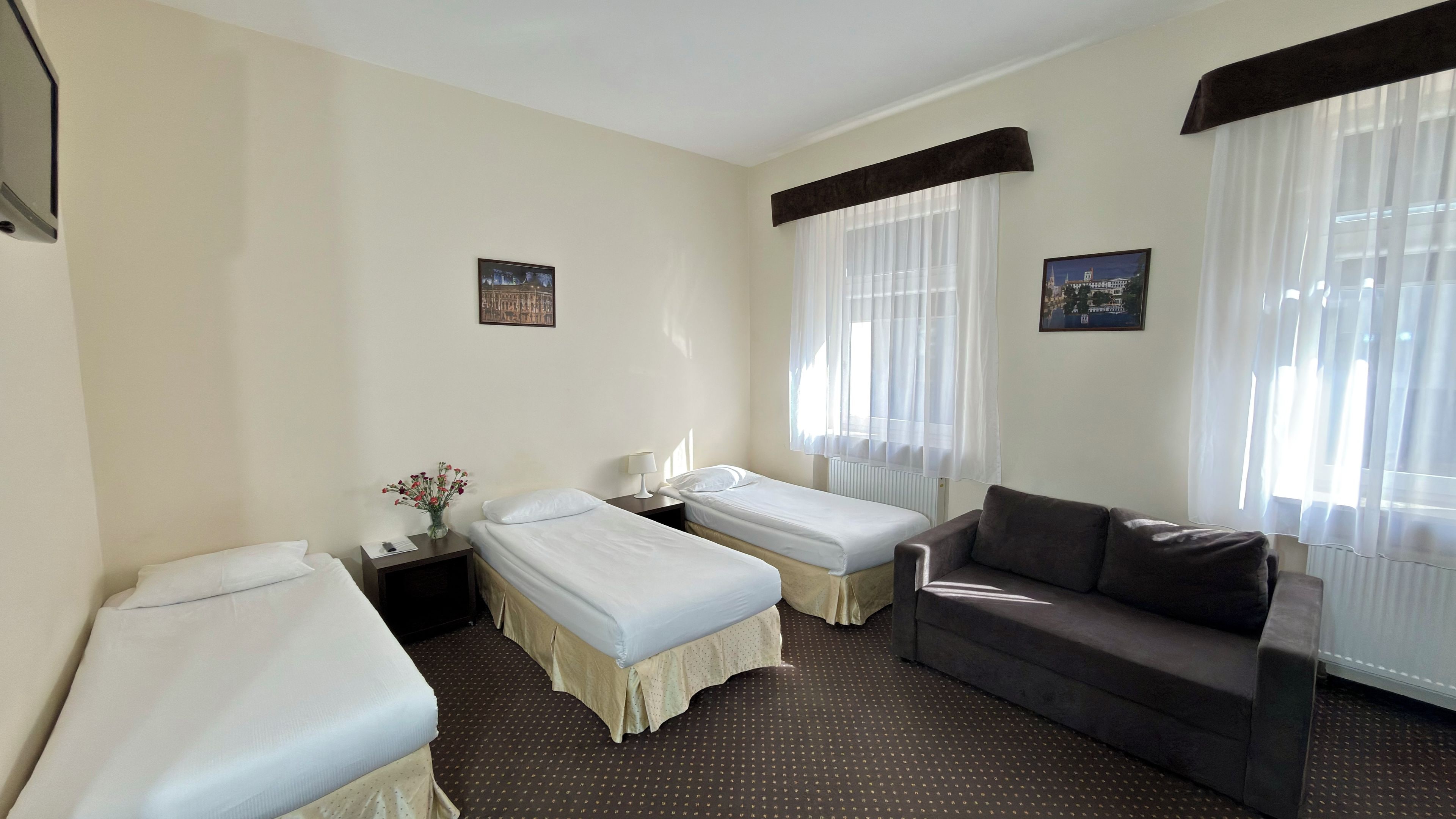 Habitación de hotel con dos camas individuales, un sofá, una mesita de noche con lámpara y un cuadro en la pared.