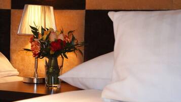 Una habitación de hotel con una cama, una mesita de noche con una lámpara y un jarrón con flores.