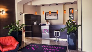 A hotel reception area with a modern design, featuring a reception desk, a red leather chair, and potted plants. - Boutique Hotel’s I Milionowa (Lodz)