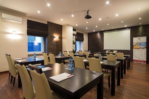 Un salón de conferencias con varias mesas, sillas y una pantalla para proyector.