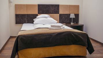 Un lit bien fait, recouvert d’une couverture marron et noire, avec des oreillers blancs et une serviette pliée posée sur le côté. On aperçoit une lampe de chevet et une petite table avec une autre lampe.