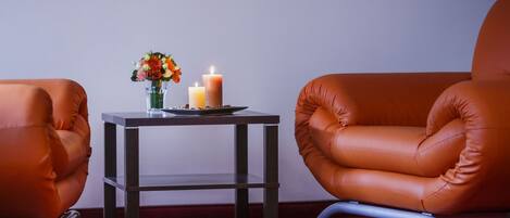 Una habitación con dos sillones de cuero, una mesita con velas y flores, y una alfombra roja.