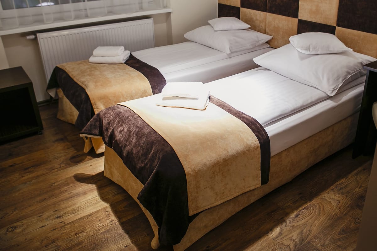 Two single beds with headboards, a bedside table, and a window with blinds.